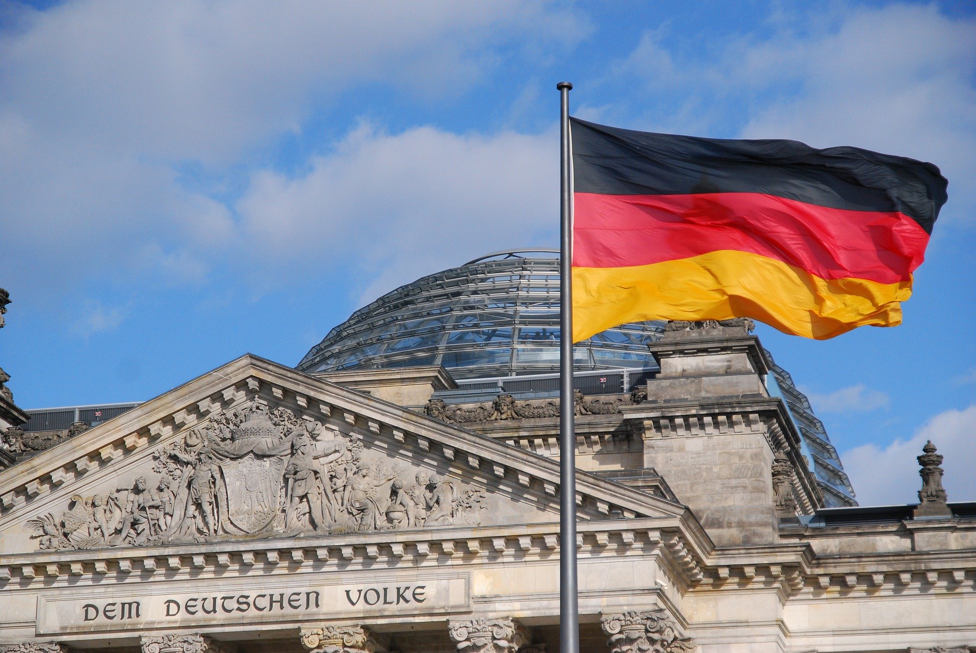 Ausschnitt des deutschen Reichstags mit Bick auf die Kuppel, davor eine deutsche Flagge im Wind